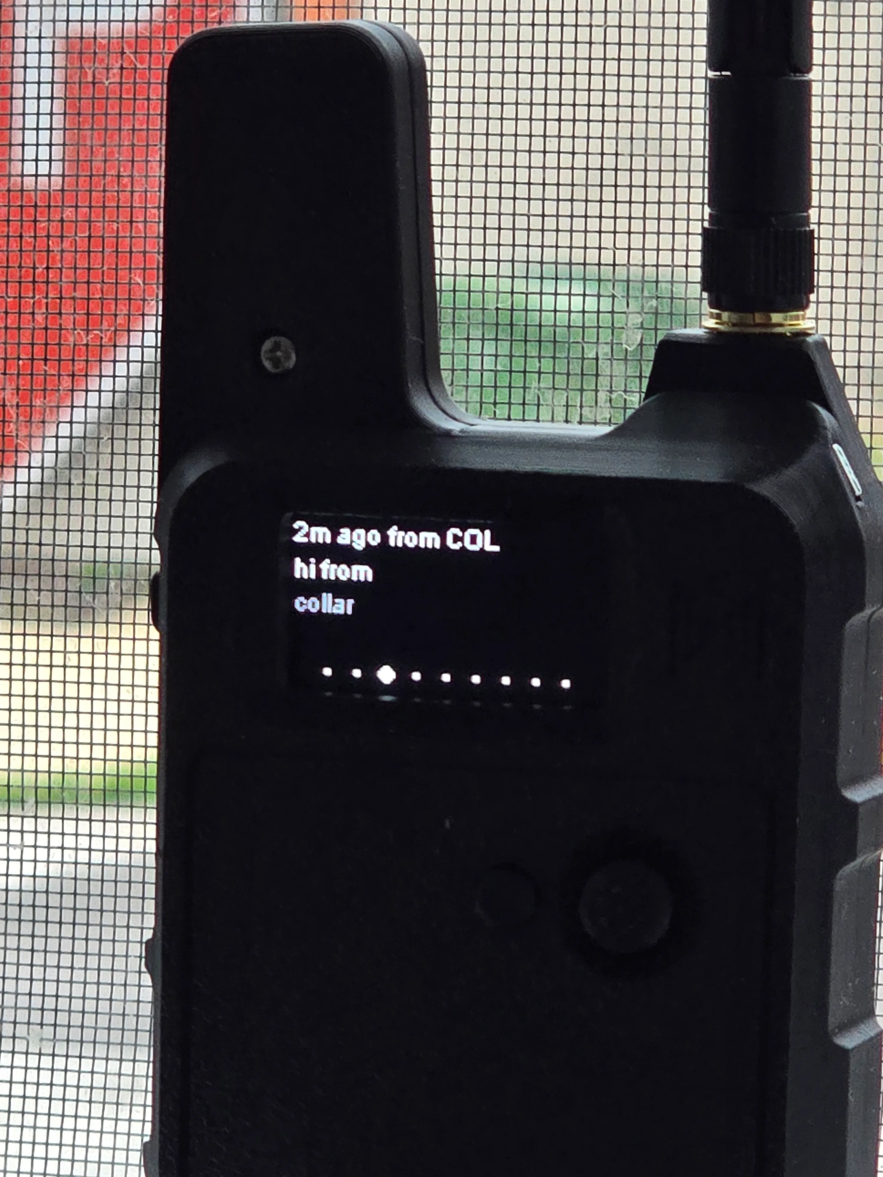 The base station node sitting in a window, its OLED showing a received message: "hi from collar," heard 2 minutes ago — proof the link carries text both directions, not just position pings.