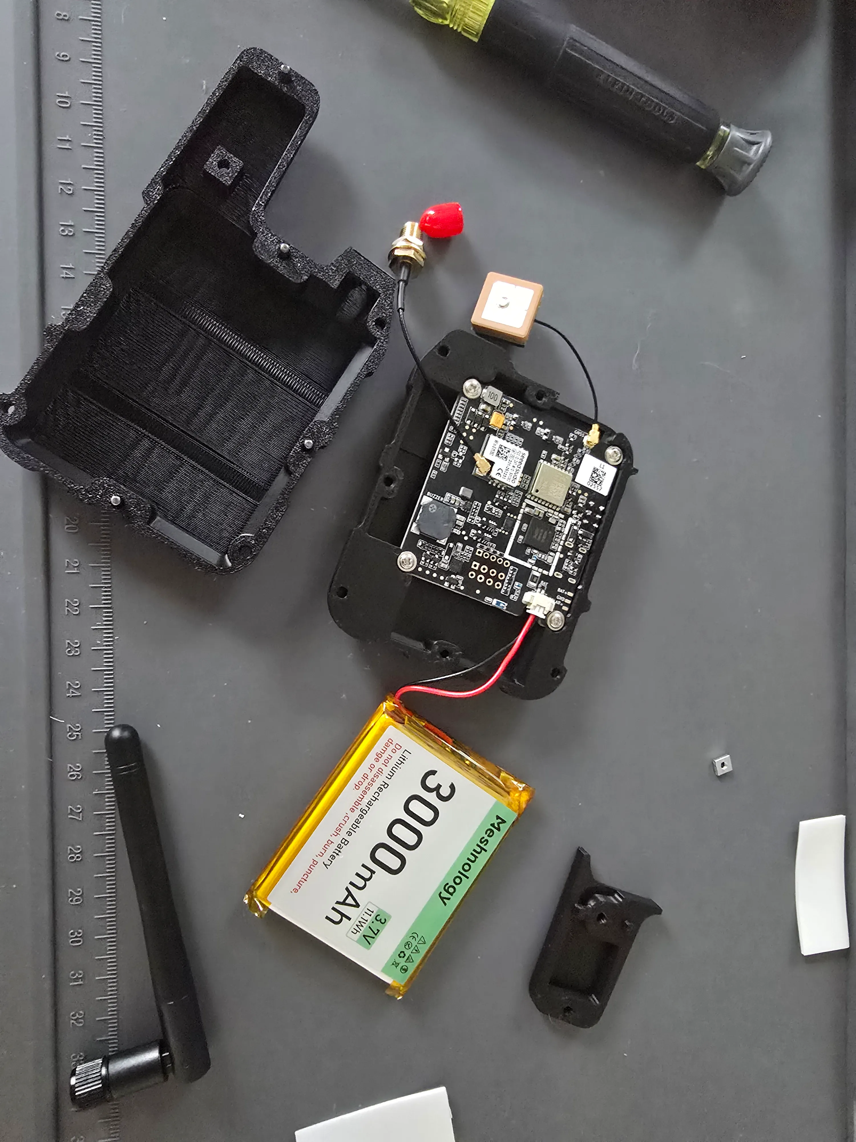 The Wio Tracker L1 wired up before closing the case: the nRF52840 plus Wio-SX1262 board with the L76K GPS patch antenna on a u.FL pigtail, an SMA LoRa antenna connector, and the 3000 mAh battery on a JST lead, resting in one half of the printed enclosure.