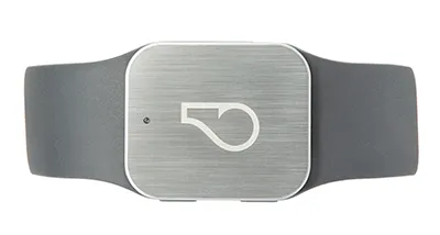 The Whistle GPS Pet Tracker itself — a rounded square of brushed aluminum stamped with the Whistle logo, threaded onto a grey rubber collar strap. The puck is barely larger than the buckle it sits next to; the cellular modem, GPS, BLE, Wi-Fi, and accelerometer all live inside that one small aluminum face.